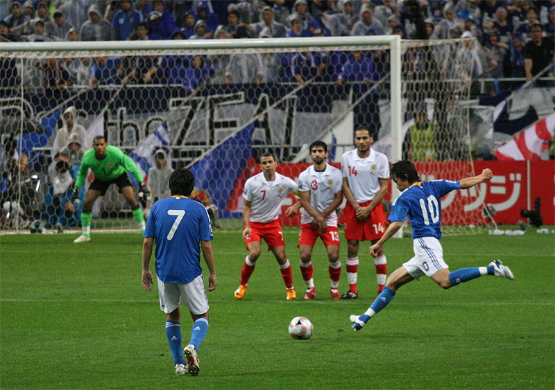 A player takes a free kick, while the opposition form a 'wall' to try to block the ball