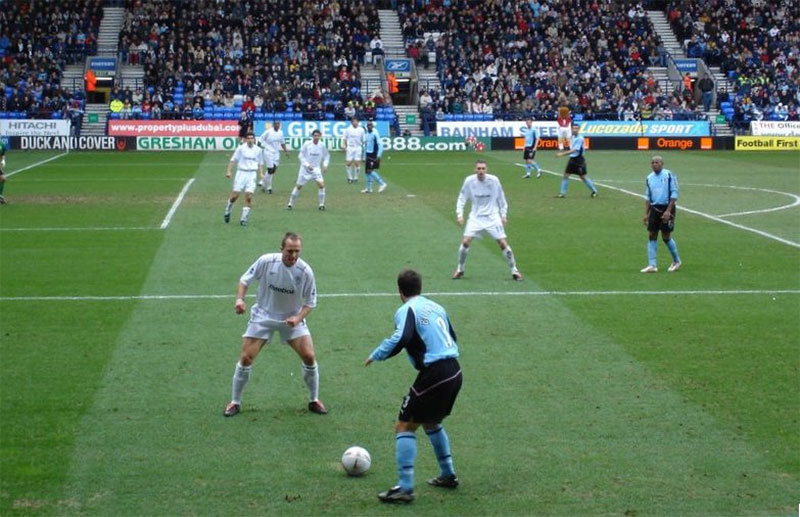 A defender (in the foreground, wearing a white shirt) challenging for possession.